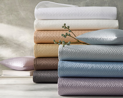 Basketweave quilted bedding stacked in an array of colors, beside a sprig of dried berries.
