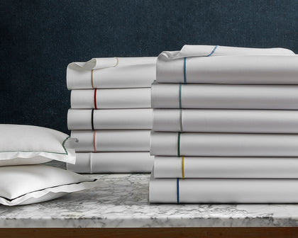 White Bergamo sheets stacked with a rainbow of trim colors, on a marble table.