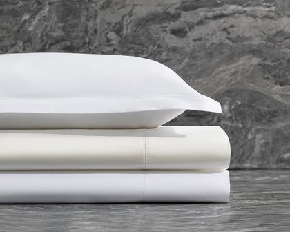 Stacked white Bergamo Hemstitch sheets with hemstitch trim against a marble backdrop.