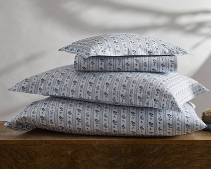 Blue and white Cabanon Stripe floral bedding stacked on a wooden table.
