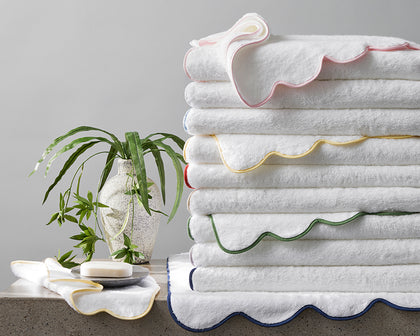 White Cairo Scallop towels with wavy scalloped trim in assorted colors, stacked beside soap and a plant.