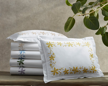 White Callista sheets stacked with floral vine embroidery in assorted colors, beside a gold-embroidered sham.