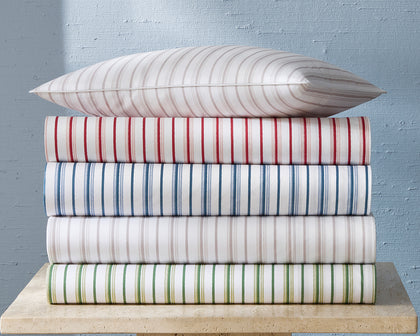 White Calypso striped sheets in assorted colors, stacked with a matching pillow.