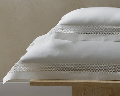 White Cecily pillows with lattice lace trim, stacked on a stone bench.