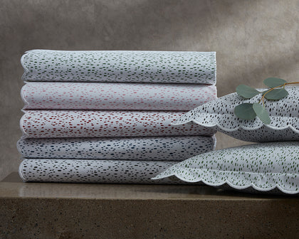 Celine speckled-print scalloped bedding in green, red, and black, stacked beside eucalyptus.