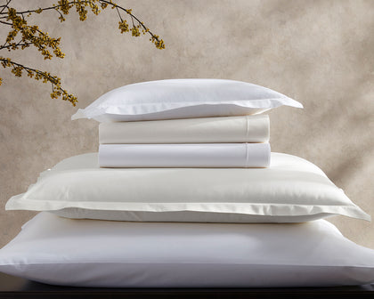 White and ivory Ceylon Satin Stitch pillows stacked, beside a flowering branch.