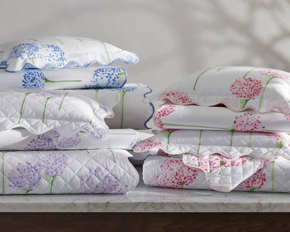 Charlotte floral quilted shams in pink, purple, and blue, stacked on a marble table.