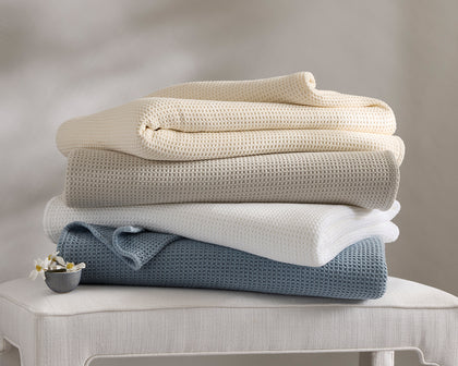 Waffle-weave Chatham blankets in tan, ivory, and white, folded and draped on a bed.