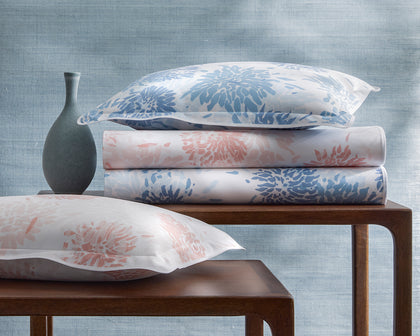 Chrysanthemum print bedding in blue and pink, stacked with matching pillows on nesting tables.
