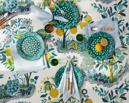 Citrus Garden print tablecloth with lemon trees, set with green textured plates and blue napkins.