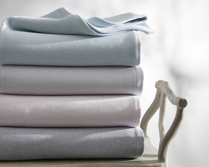 Costa Mesa textured blankets in pale blue, gray, and pink, stacked on a chair.
