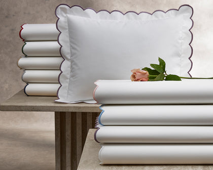 White Dakota scalloped sheets stacked with colorful edge trim, topped with a pink rose.