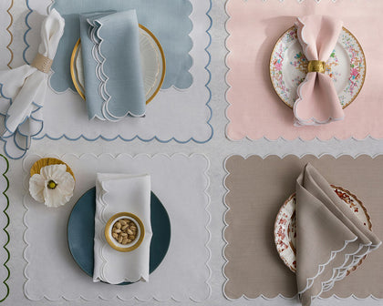 Dakota scalloped placemats in blue, pink, white, and tan, each set with a plate and napkin.