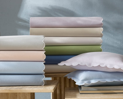Diamond Pique scalloped sheets in pastel colors, stacked with matching pillows on side tables.