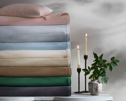 Dream Modal sheets stacked in a rainbow of solid colors, beside candles and greenery.