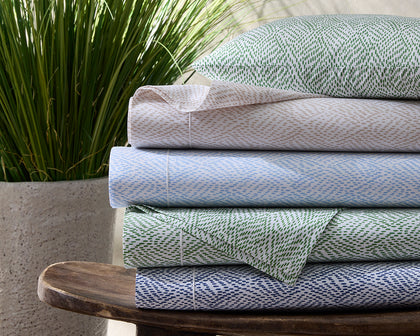 Duma Diamond print sheets in green, tan, blue, and navy, stacked on a wooden stool.