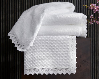 Ellis white lace-trim towels and bath mat stacked with an orchid