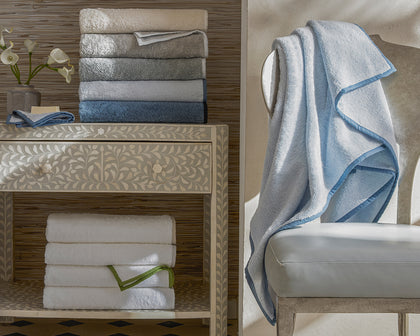 Enzo bath towels in a gray to blue gradient stacked on a console table.
