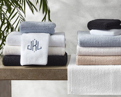 Francisco ribbed towels stacked in gray, white, tan, and black with a monogrammed washcloth.