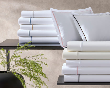 White Gatsby bedding stacked with contrast piping in various colors and pillow shams with pink and black trim.