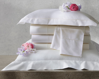 Ivory Gatsby hemstitch bedding stacked with pillow shams and fresh flowers.