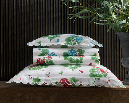 White Geranium print bedding stacked with scalloped edges in blue and red floral patterns.