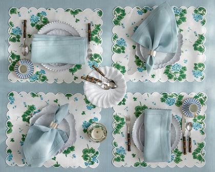 White and blue Geranium print placemats set with blue napkins and white plates, seen from above.