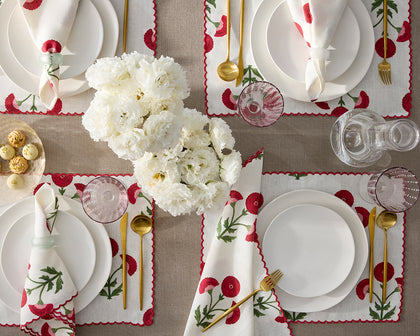 White Gisele placemats embroidered with red poppies, set with white plates and gold flatware, seen from above.