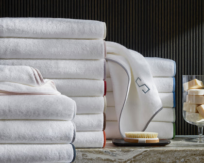 White Giza towels stacked with a monogrammed washcloth draped in front and soaps in a glass.
