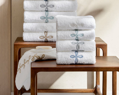 White Gordian Knot towels stacked with embroidered knot borders in blue and gold, on a wooden table.