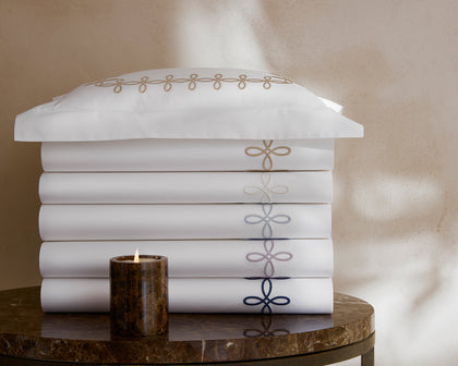 White Gordian Knot bedding stacked with an embroidered border in shades of gold, gray, and navy.