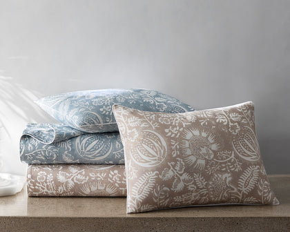 Granada floral print sheets and a sham in blue and tan, stacked on a stone surface.