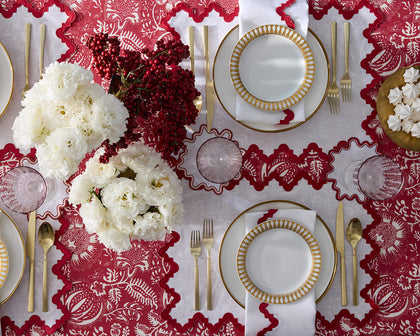 Red Granada floral print scalloped placemats set with gold-rimmed china, white ranunculus, and berries.