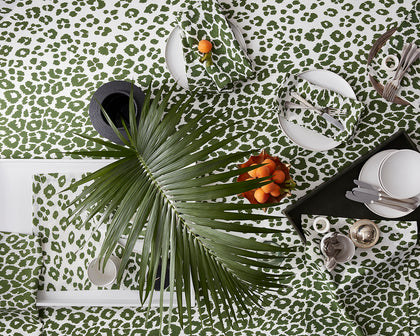Green Iconic Leopard print tablecloth and napkins set with white plates, a palm frond, and apricots.