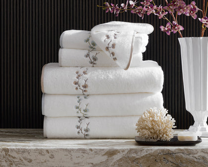 White Jasmine Giza towels with an embroidered floral vine, stacked beside a coral decoration and orchid stems.