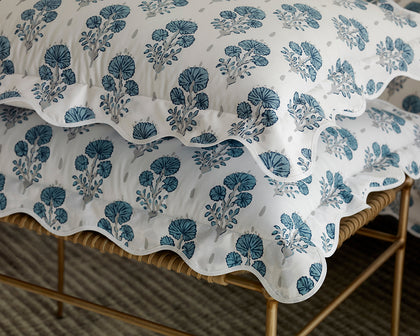 Blue Joplin floral print scalloped pillows stacked on a woven bench.