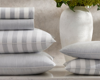 Lana grey striped sheets and pillows stacked beside a vase