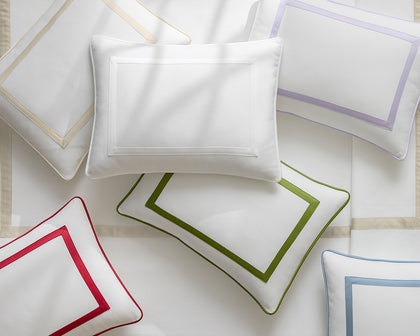 White Louise Pique pillows with bordered trim in red, green, lavender, and tan, arranged flat.