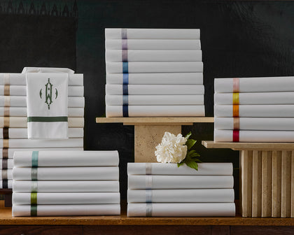 White Lowell sheets stacked with ribbon trim in a rainbow of colors, one monogrammed.