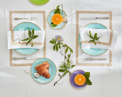 White Lowell tan-bordered placemats set with turquoise plates, croissants, and citrus.