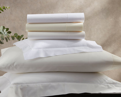 White and ivory Luca Hemstitch sheets stacked with hemstitch trim, beside a eucalyptus sprig.