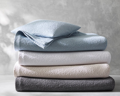 Malibu textured bouclé bedding stacked in blue, gray, tan, and charcoal.