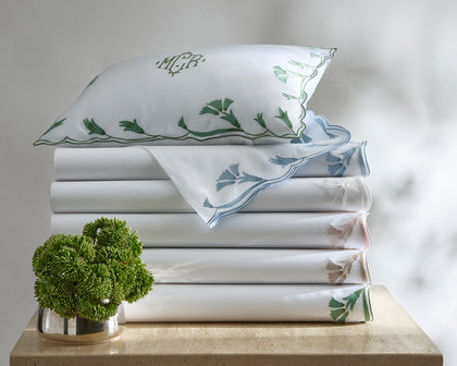 White Marcella sheets with vine-embroidered scalloped trim in assorted colors, stacked with a monogrammed pillow.