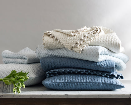 Margaret textured quilted bedding with pompom trim, stacked in ivory and shades of blue.