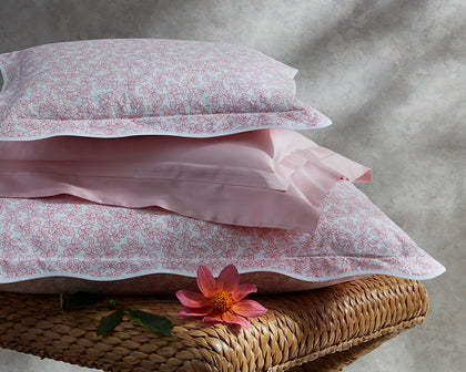 Pink Margot vine-print scalloped bedding stacked on a woven bench.