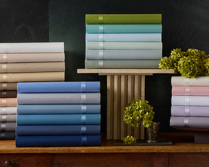 Nocturne sateen sheets stacked in assorted colors on a wood console with hydrangeas.
