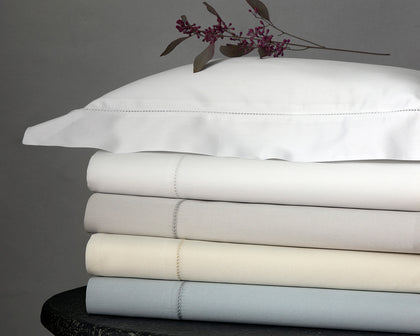 Nocturne Hemstitch sheets stacked in assorted colors on a stone stool with a berry sprig on top.