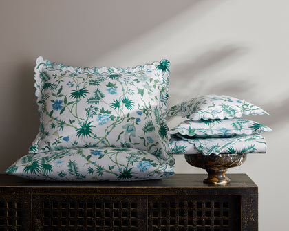 White Palmyra floral-print pillows with scalloped edges stacked on a carved dark console.