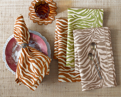 Zebra-print Regine napkins in orange, green, and tan set on a woven placemat with floral china.