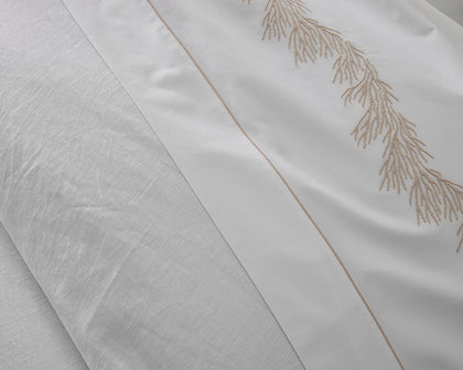 White Roman Hemstitch sheet with a beige branch-embroidered border, folded beside a linen pillow.